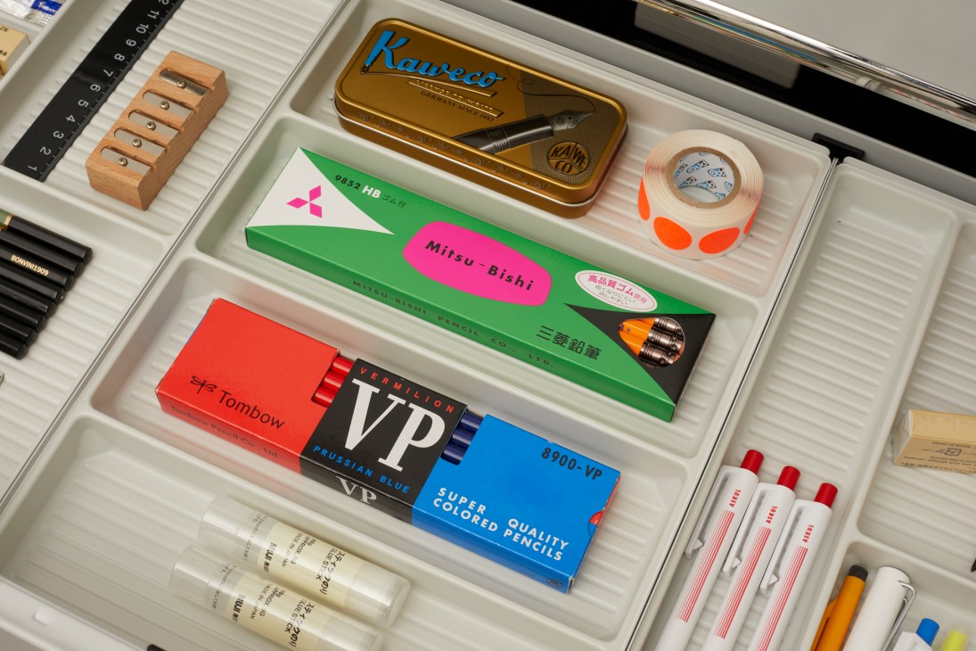 Kaweco fountain pen in gold tin box displayed with other stationery items including Mitsubishi and Tombow pencils in an organized drawer.