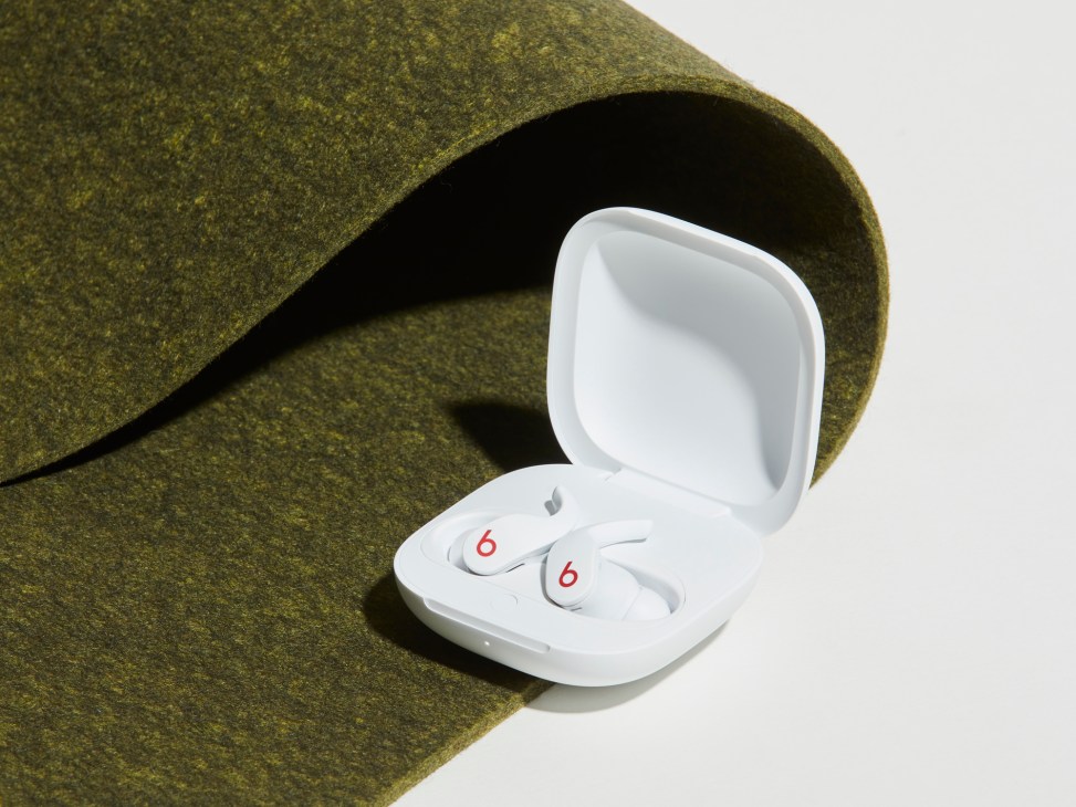 White Beats Fit Pro wireless earbuds in charging case next to rolled green fabric showing wingtip design