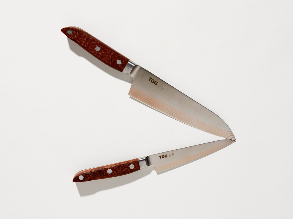 Two TOG knives with layered steel blades and wooden handles crossed against white background