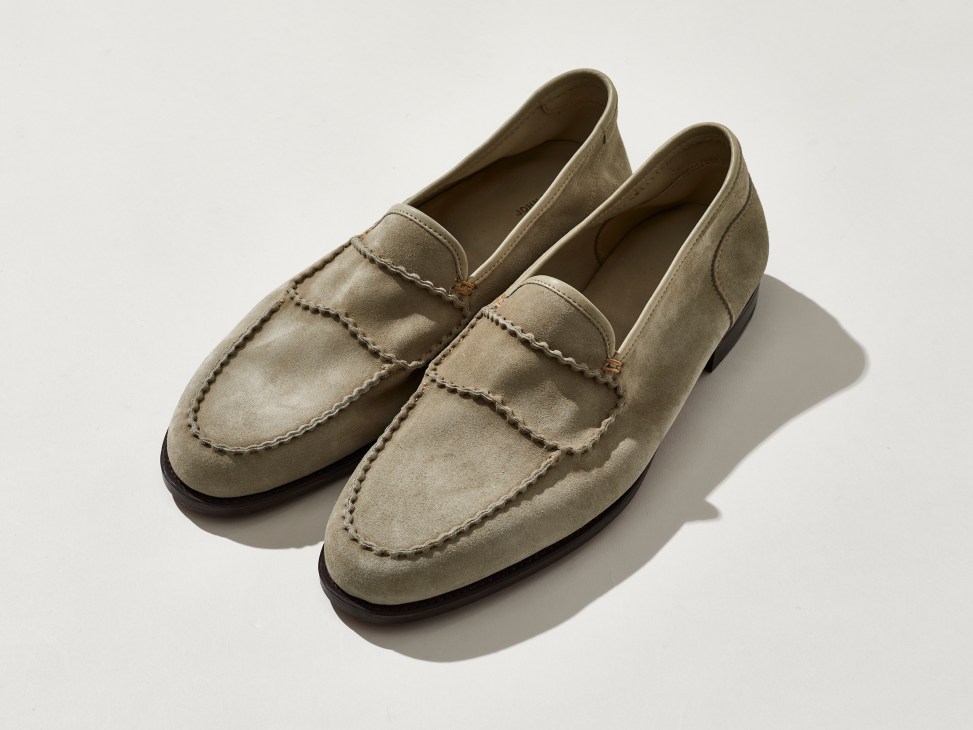 Beige suede loafers with moccasin stitching and dark rubber soles photographed on white background