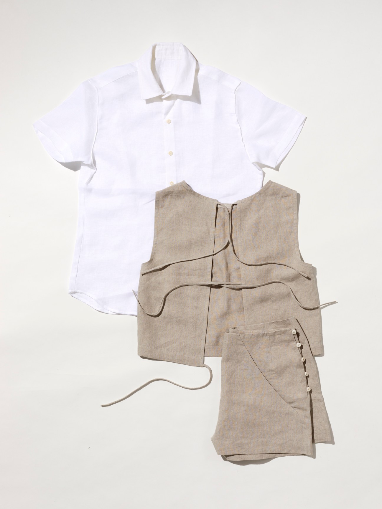 White linen shirt and beige linen vest laid flat on neutral background