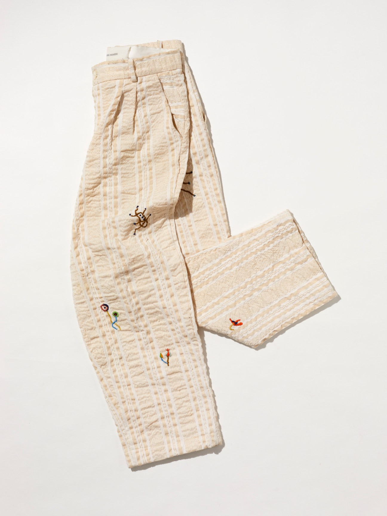 Cream colored textured pants with small colorful embroidered details scattered across the fabric
