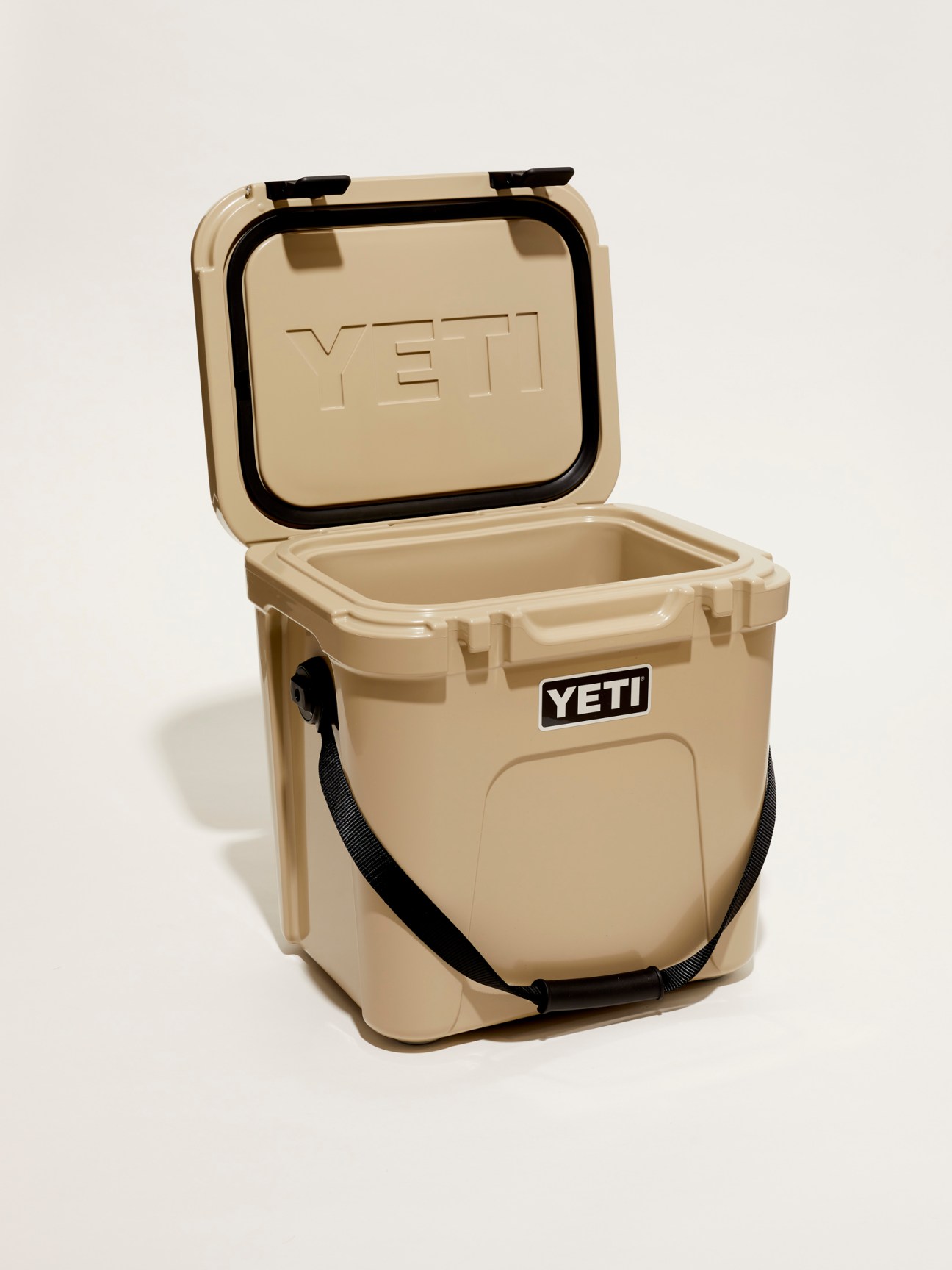 Tan Yeti cooler box with black handles and latches, lid open showing empty interior