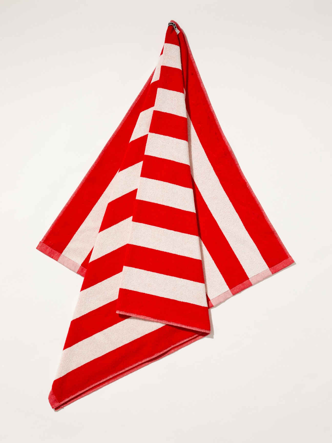 Red and white striped beach towel by Hommey hanging against white background