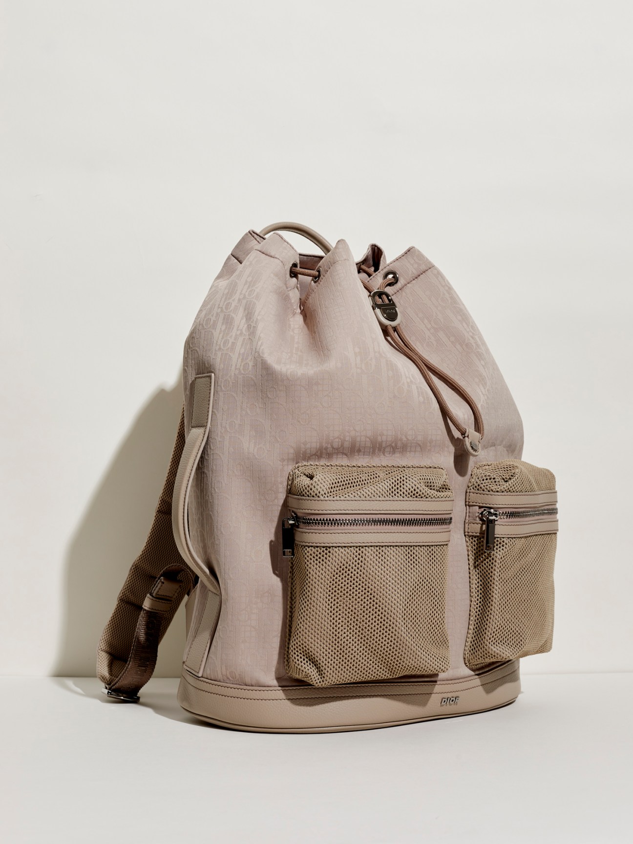 Beige drawstring backpack with mesh pockets and adjustable straps on neutral background