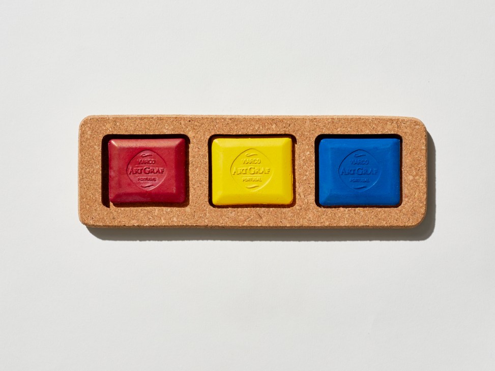 Three square colored blocks in red, yellow, and blue set in a cork holder against a white background