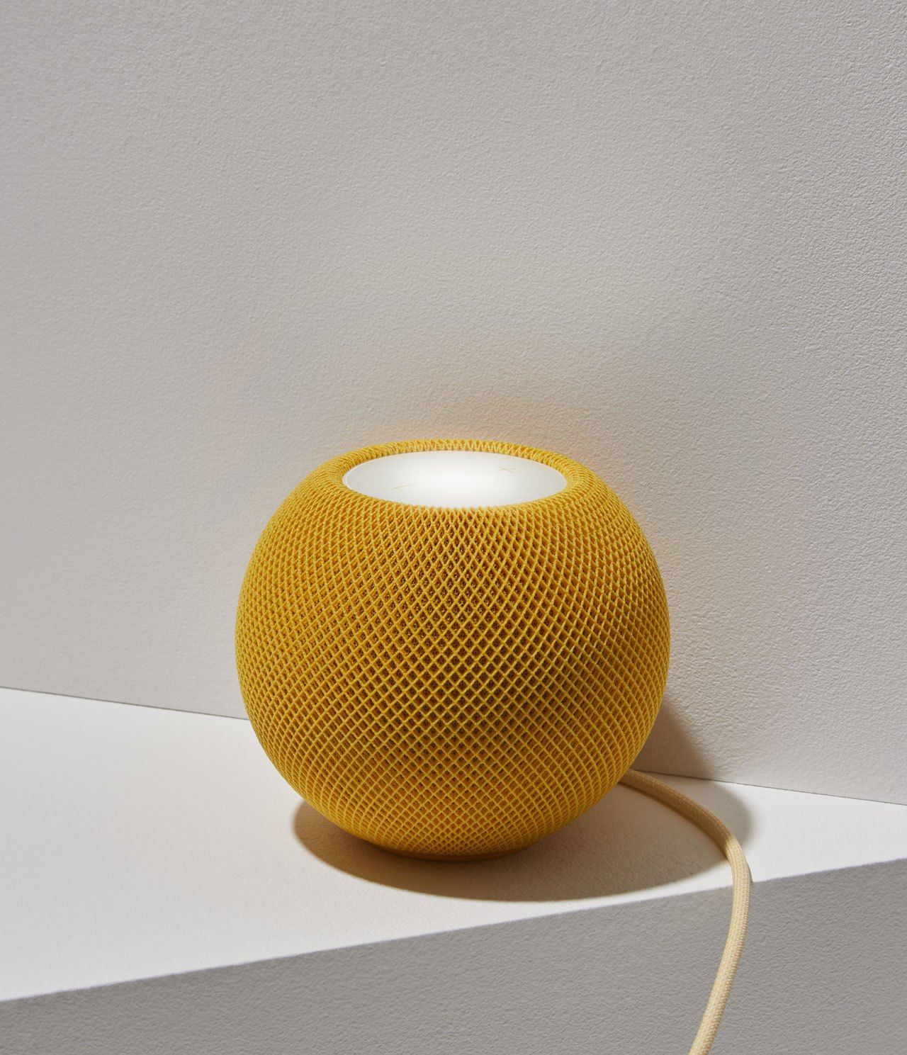 Yellow knitted smart speaker with open top and power cord on white surface