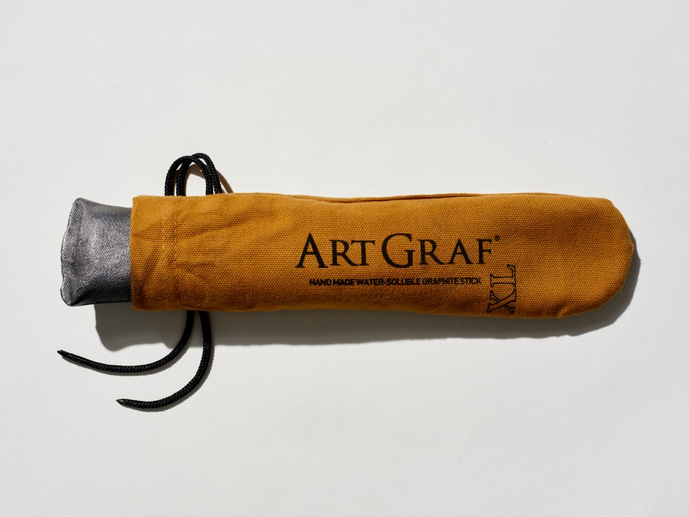 Orange cylindrical ArtGraf XL graphite stick with black cord and gray cap against white background