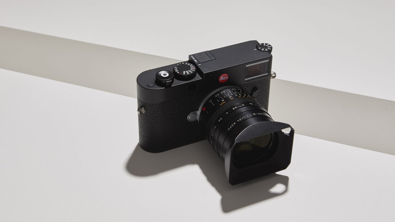 Black Leica M rangefinder camera with lens and hood on white surface