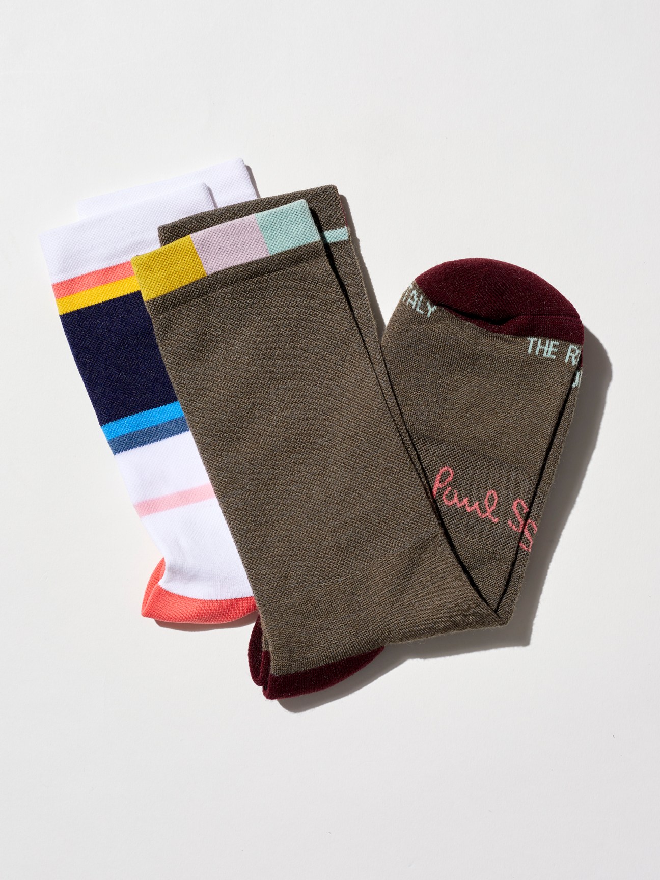 Two pairs of Paul Smith Artist Stripe cycling socks with colorful stripes- one with colorful stripes on white background, one olive green with burgundy heel