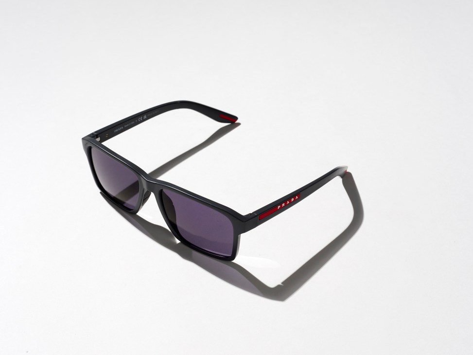 Black rectangular Prada cycling sunglasses with dark lenses and red detailing on the temples against white background