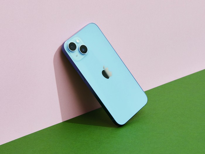 Apple iPhone 14 in blue positioned diagonally against pink and green geometric background