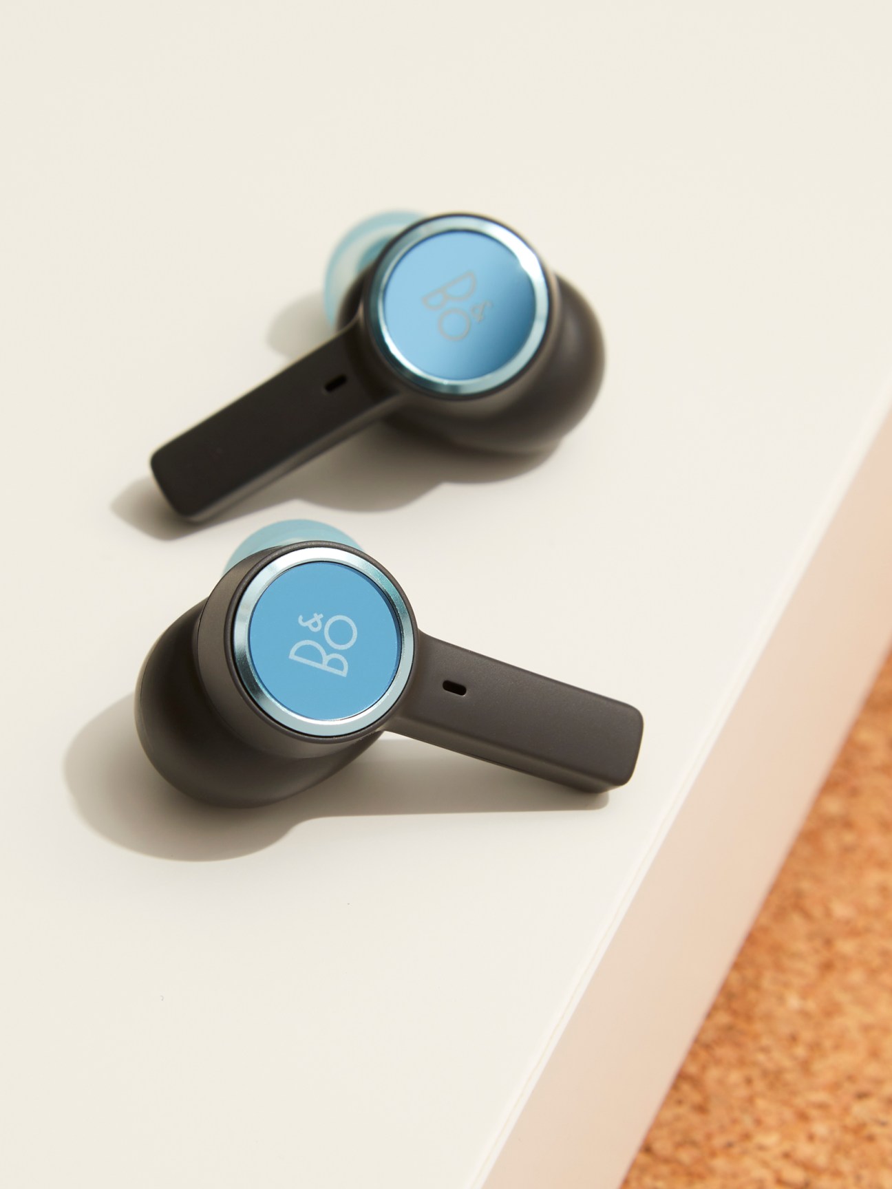 Bang & Olufsen Beoplay EX wireless earbuds with blue circular face plates and black stems on white surface