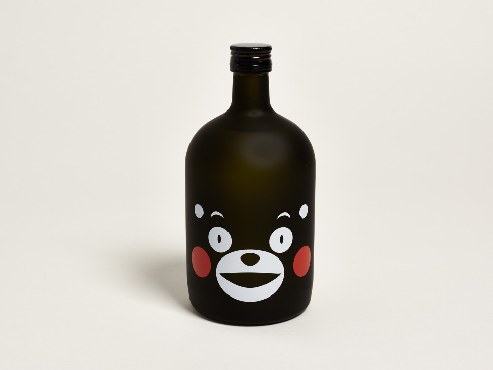 Dark glass bottle of Kurahachi shochu featuring Kumamon's cheerful bear face design with white eyes and red cheeks