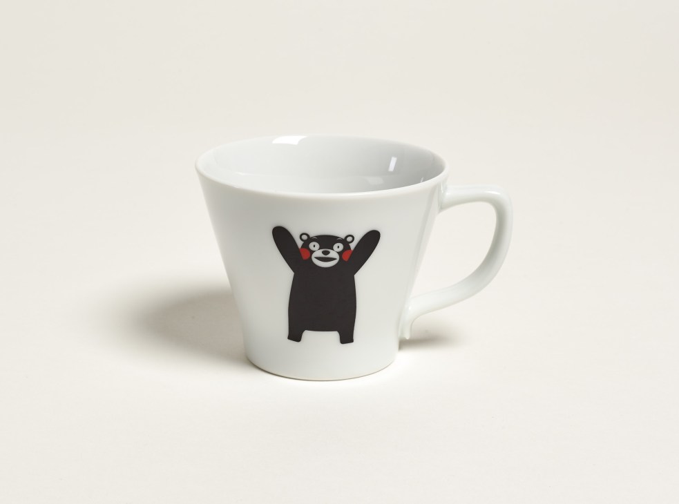 White ceramic cup with black bear mascot Kumamon design featuring arms raised and red cheeks