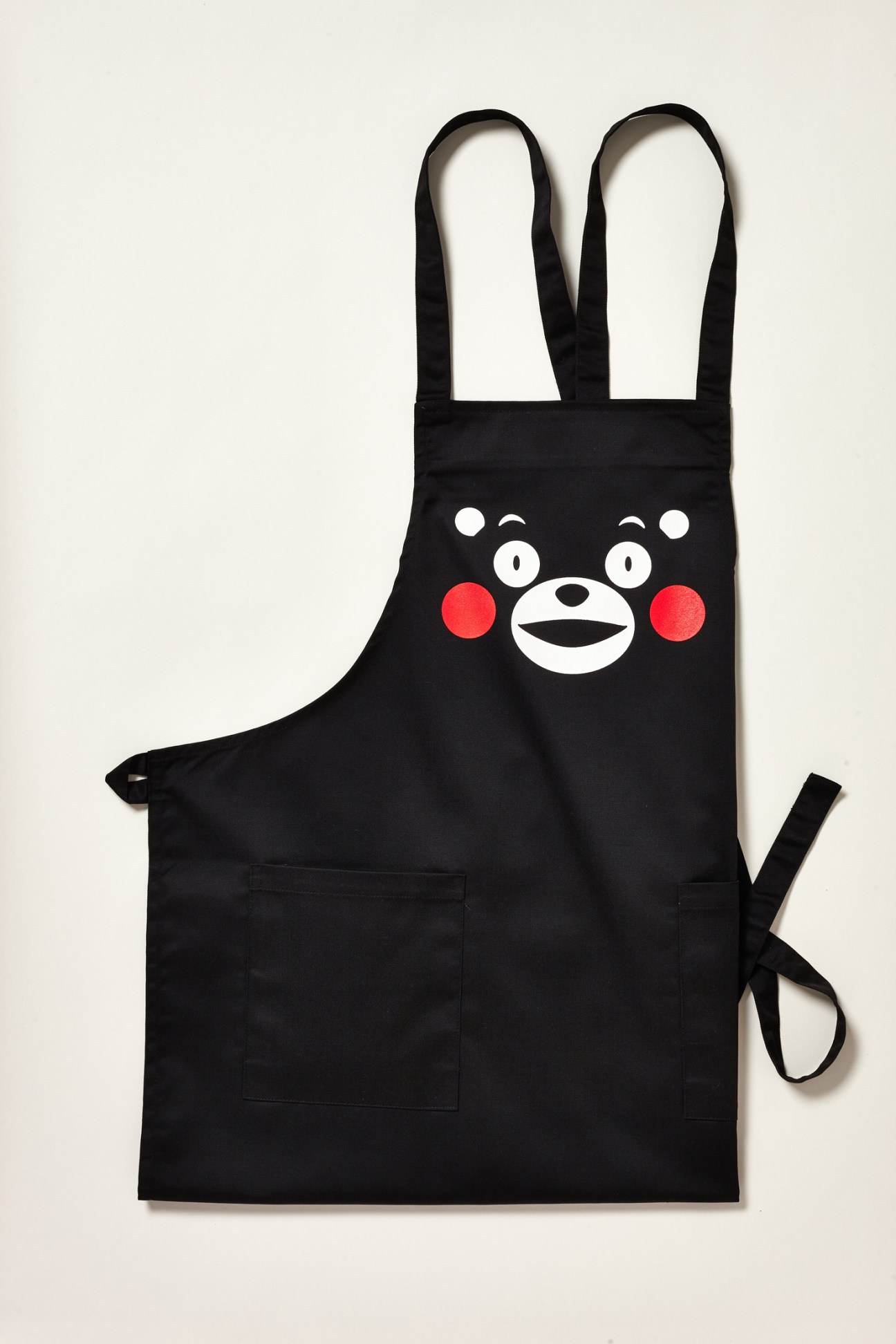 Black kitchen apron with Kumamon's cute bear face design featuring white eyes, red cheeks and cheerful expression