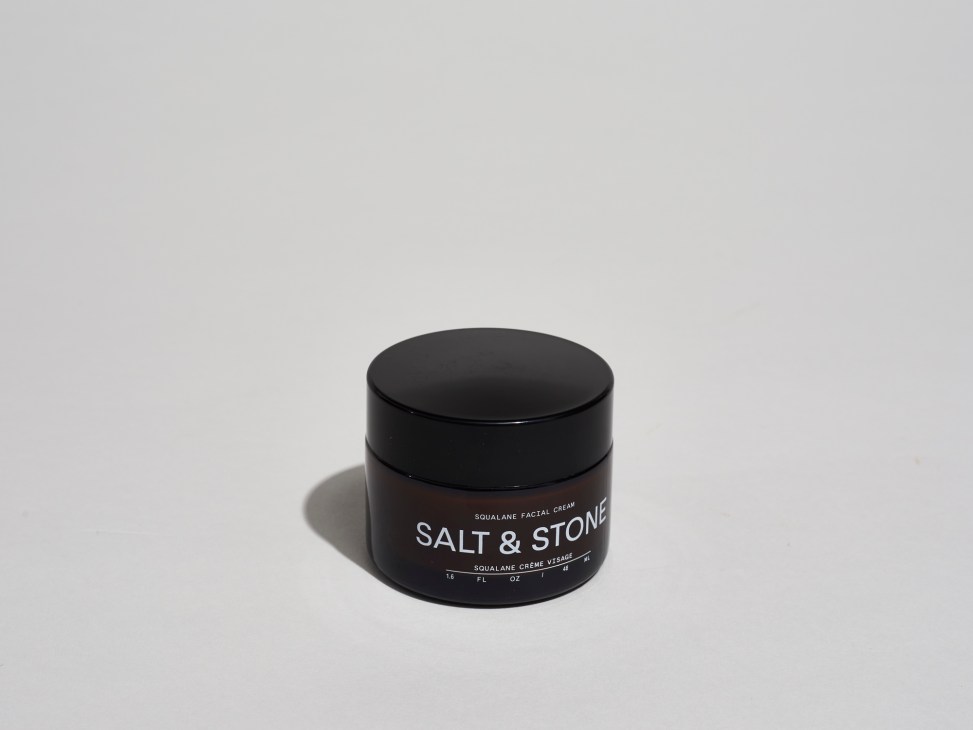 Salt & Stone squalane facial cream in a black glass jar on grey background.