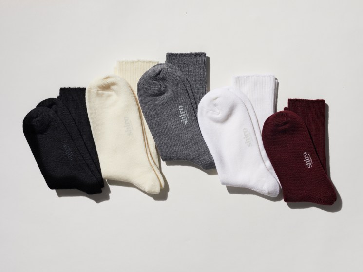Five folded crew socks in black, cream, gray, white, and burgundy colors arranged on white background