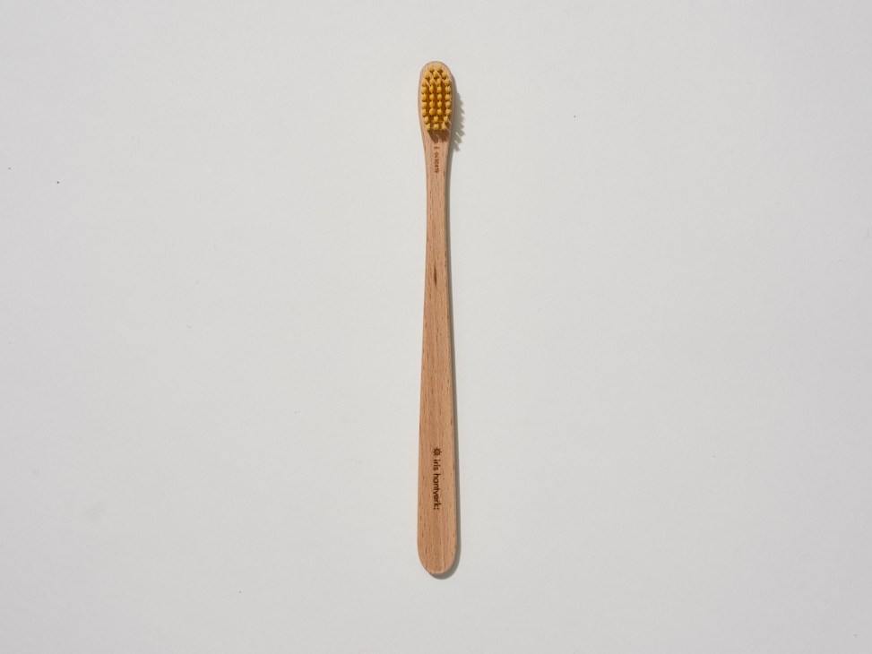 Wooden toothbrush with gold bristles by Iris Hantverk against a light background.