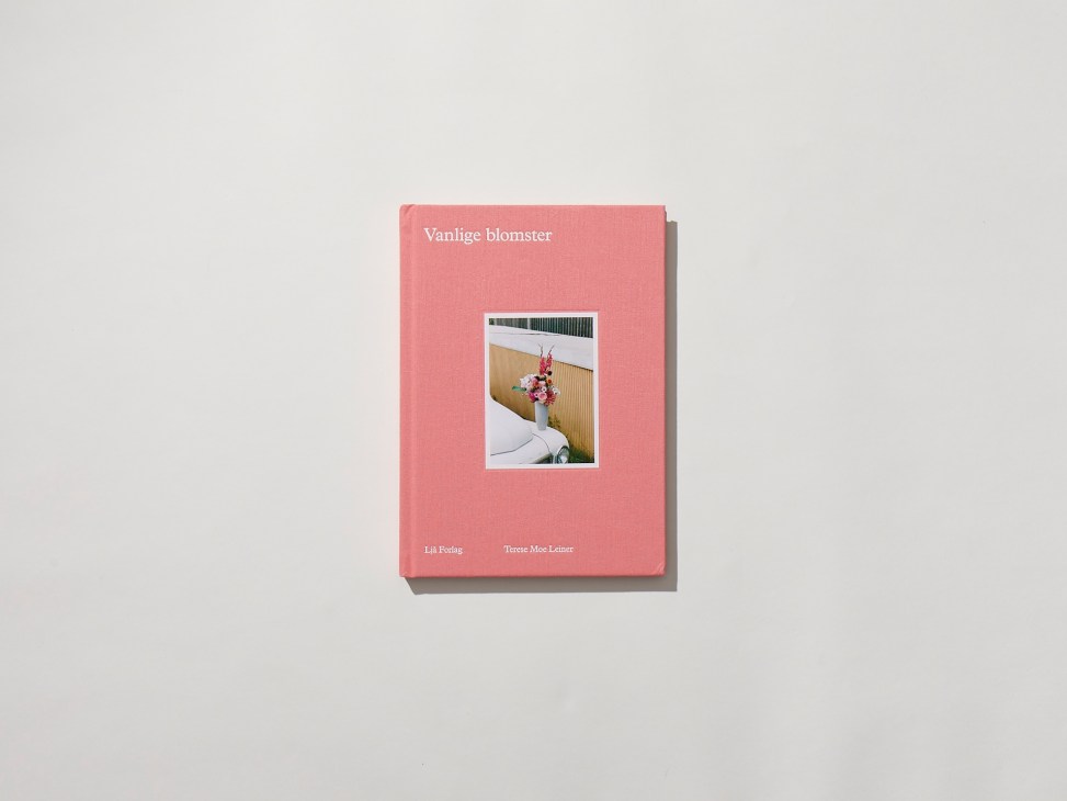 Pink book cover with photograph of flowers in vase next to bed, titled Vanlige blomster