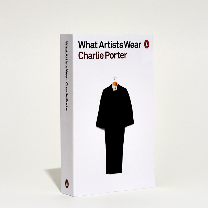 Book cover of 'What Artists Wear' by Charlie Porter featuring a black coat on a hanger against white background.