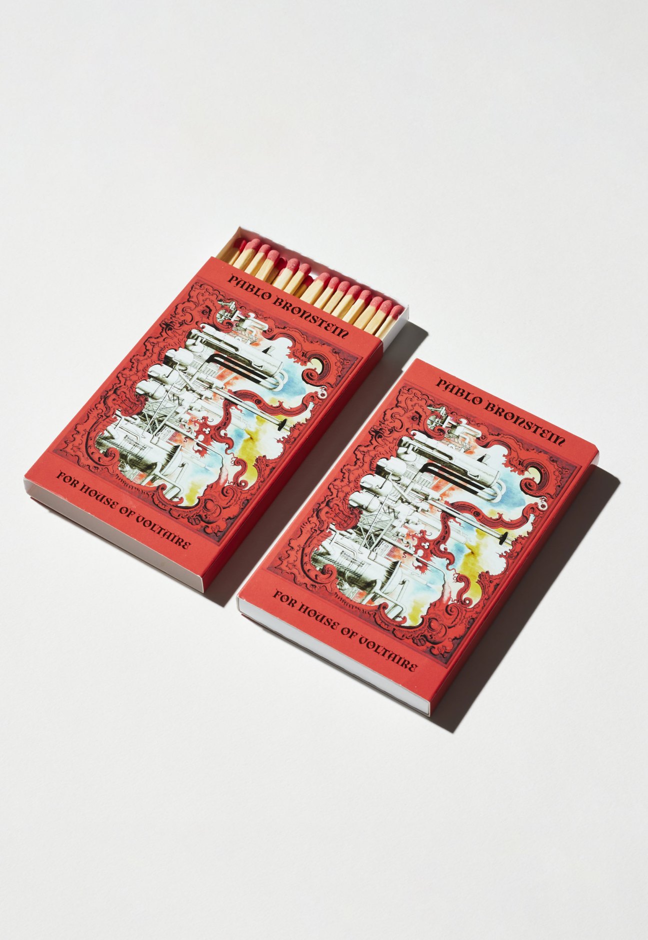 Two red matchboxes with Pablo Bronstein design and decorative ornamental patterns.