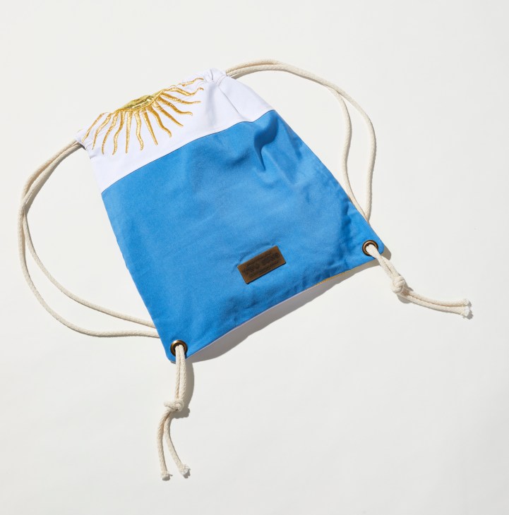Blue drawstring backpack with white and gold eyelash design by Adrián Villar Rojas.