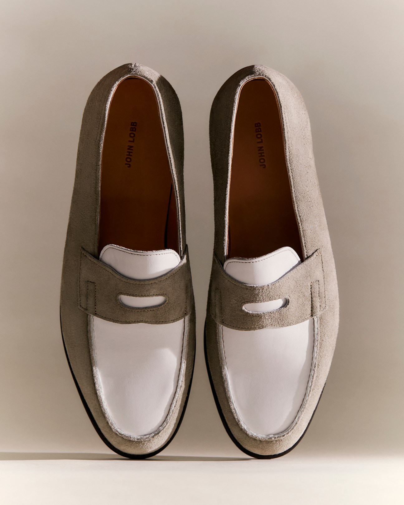Pair of two-tone suede loafers in beige and white with penny strap detail on neutral background
