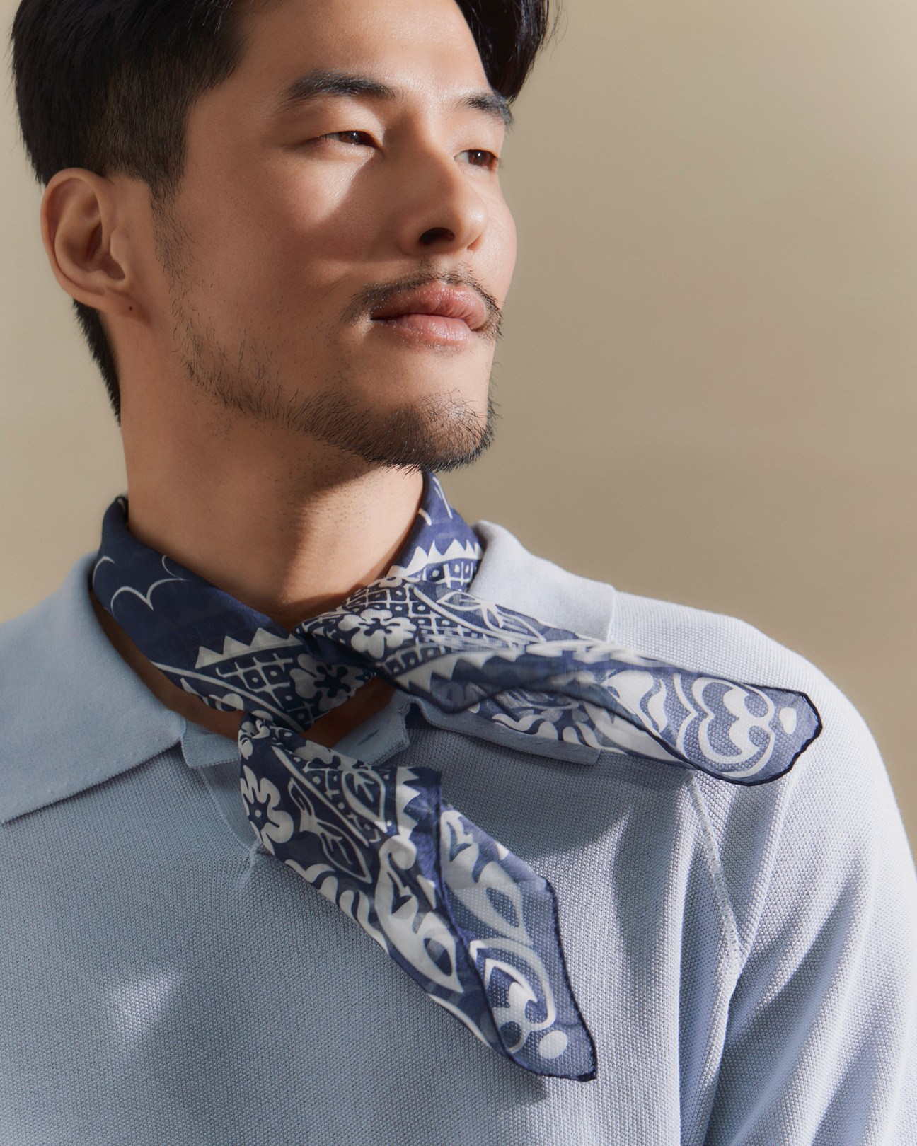 Asian man wearing light blue polo shirt with patterned blue and white bandana tied around neck