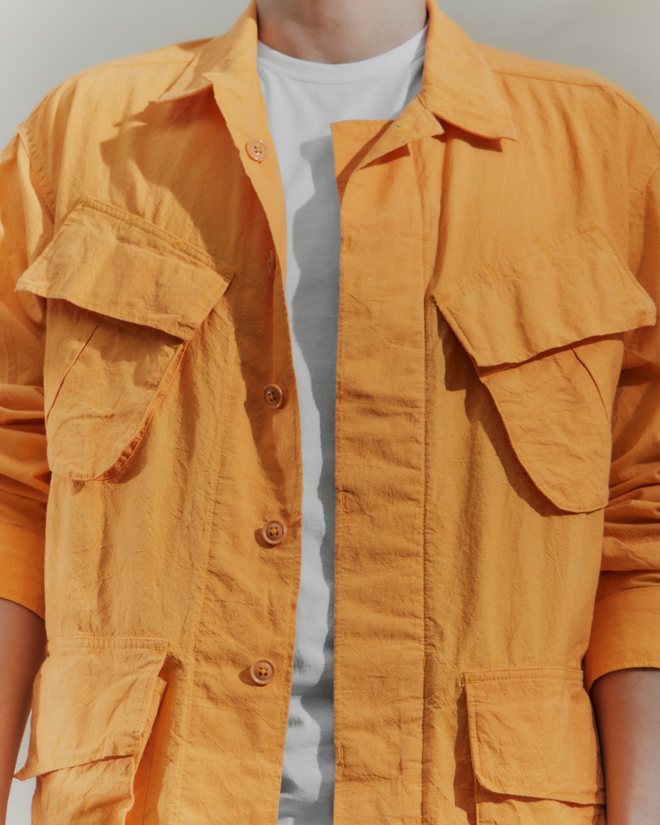 Person wearing open mustard yellow utility jacket with multiple pockets over white t-shirt