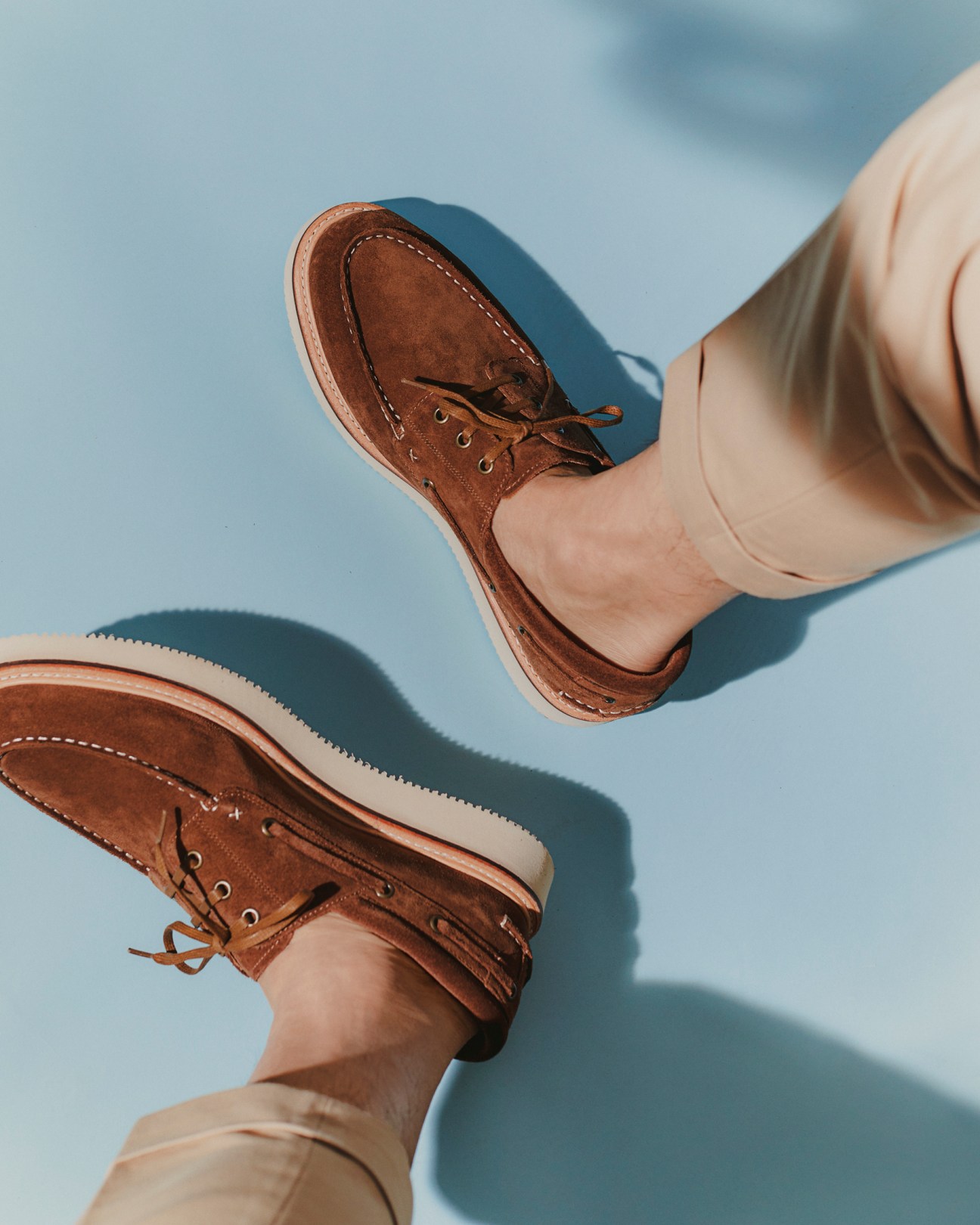 Person wearing brown leather boat shoes and beige trousers against cloudy sky background