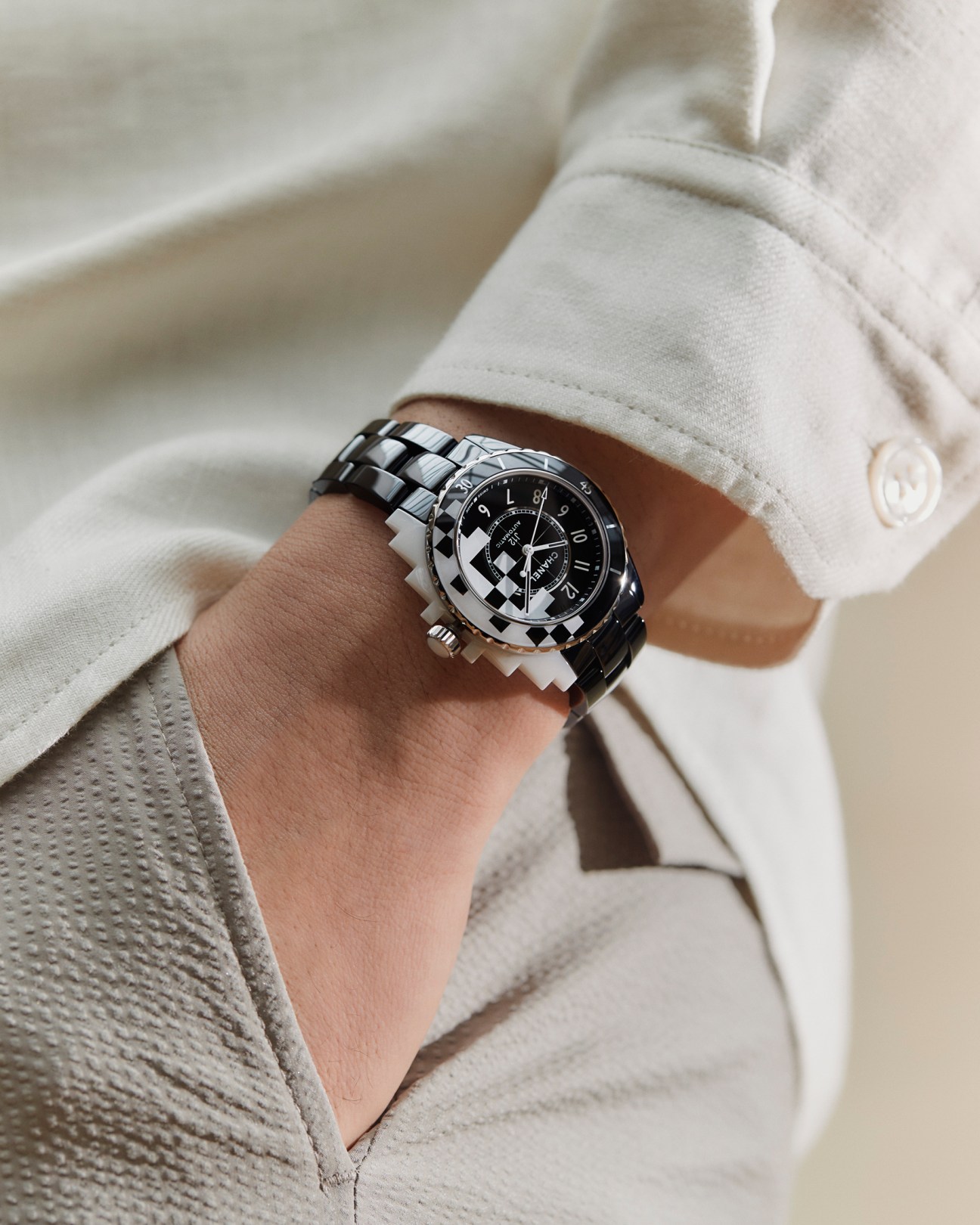 Close-up of person wearing white shirt and beige trousers with black and silver Chanel J12 watch on wrist