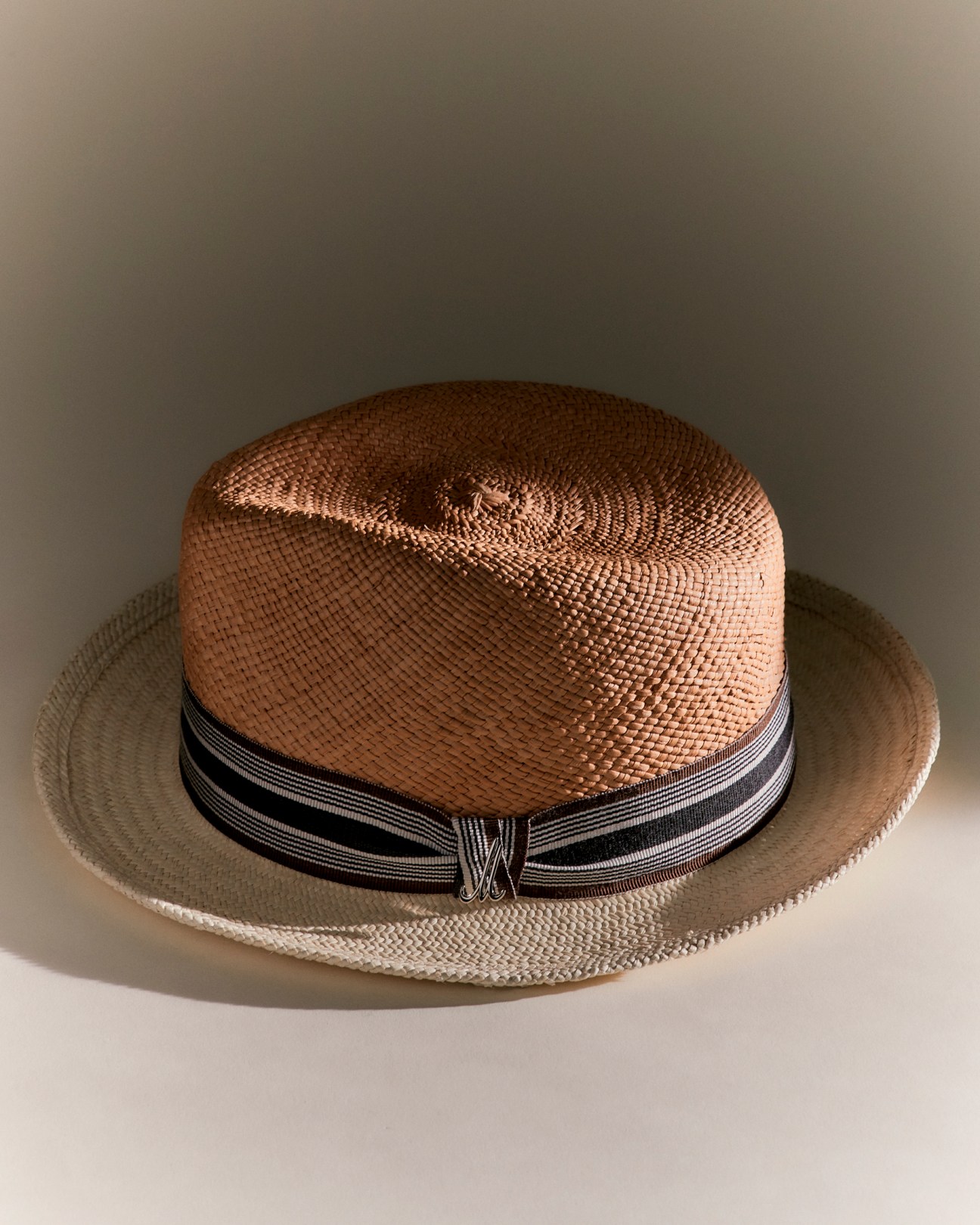 A woven straw fedora hat with black and white striped band and metal accent, photographed against neutral background