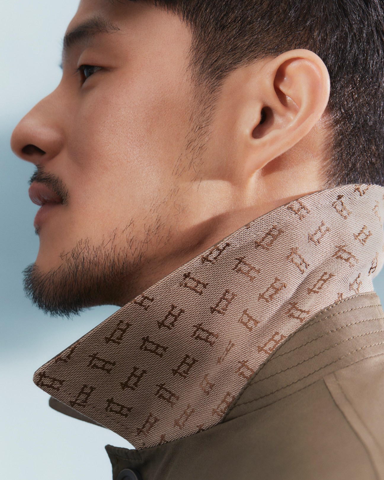 Profile view of Asian man wearing beige Herno coat with brown monogram pattern collar detail