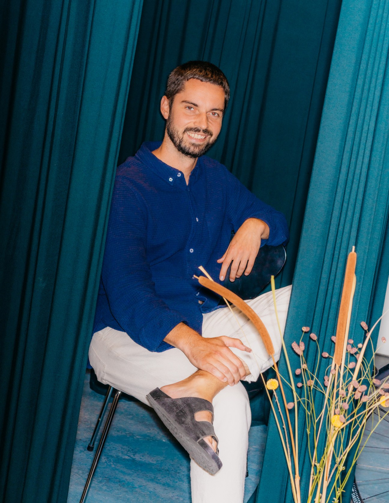 Thies Meyer, co-founder of About Companions, sitting in blue shirt in Berlin studio with teal curtains