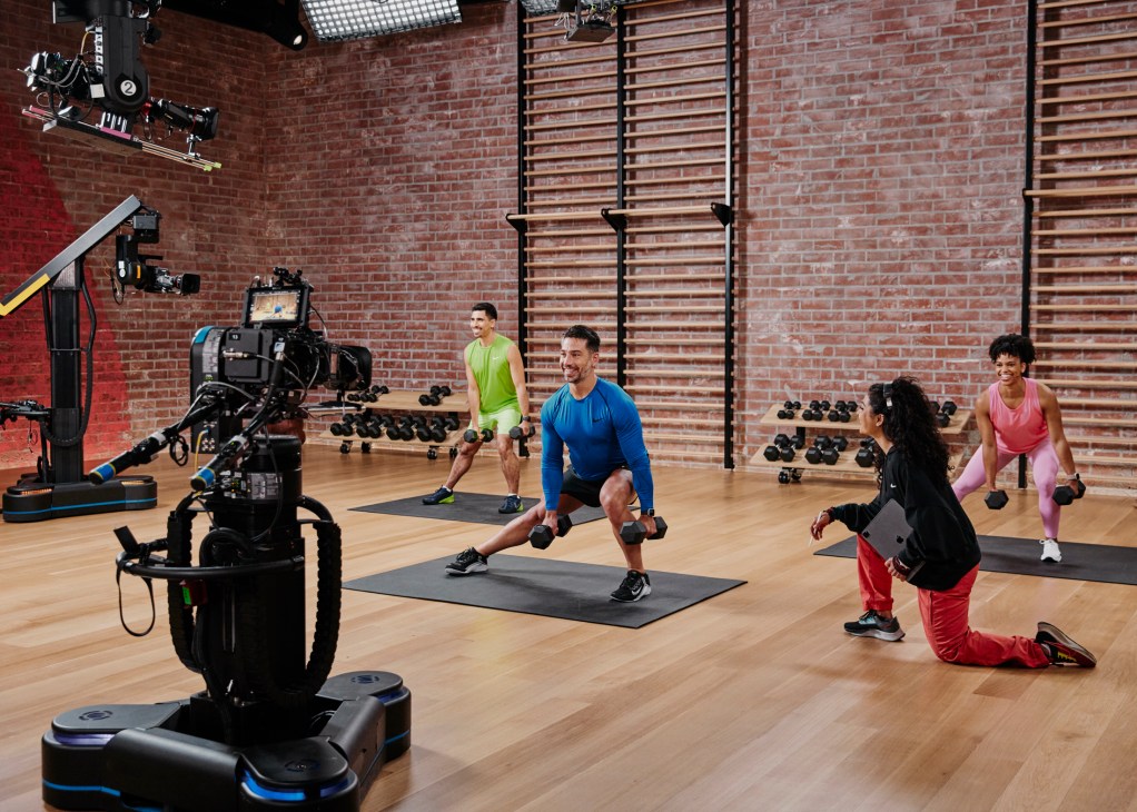 Fitness trainers exercising in Apple Fitness+ studio with professional cameras and lighting equipment