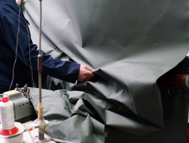 Person in blue jacket using steam iron on dark waxed cotton fabric in textile manufacturing facility