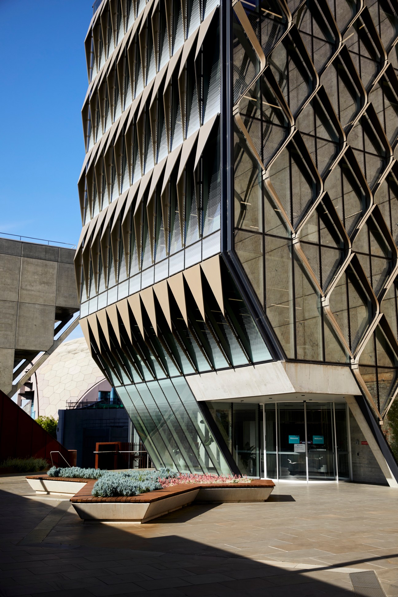 Modern angular building with geometric metal lattice facade and glass panels overlooking waterfront.