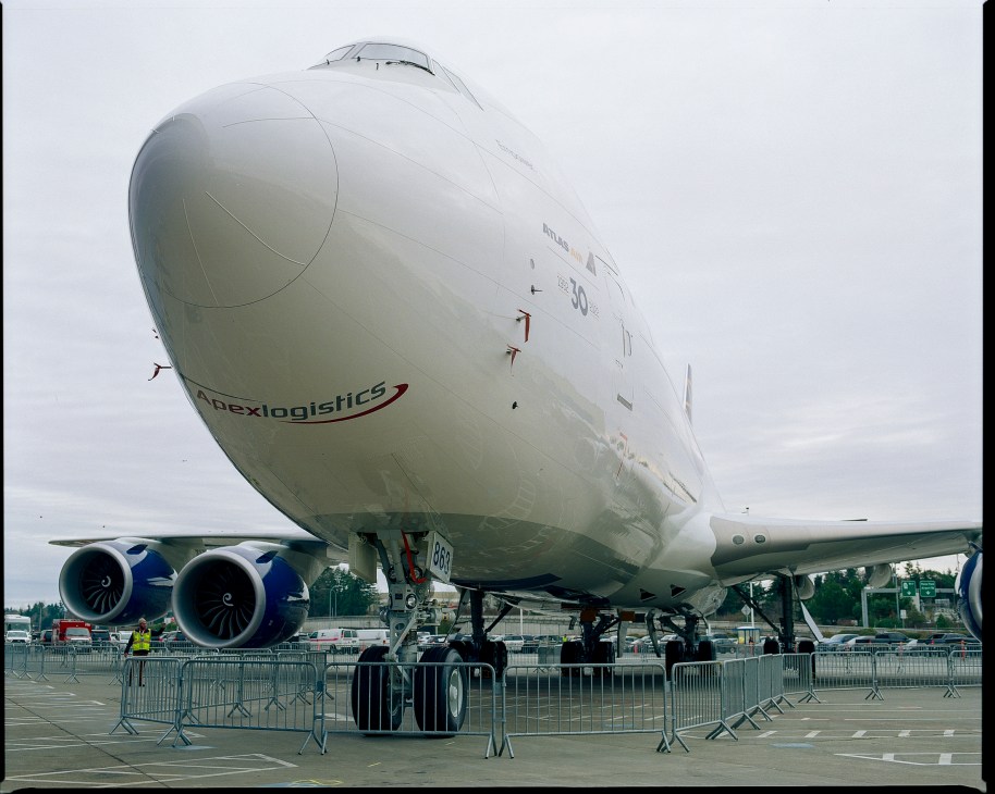 Close-up view of white Boeing 747 jumbo jet nose and engines on display behind metal barriers at aviation show