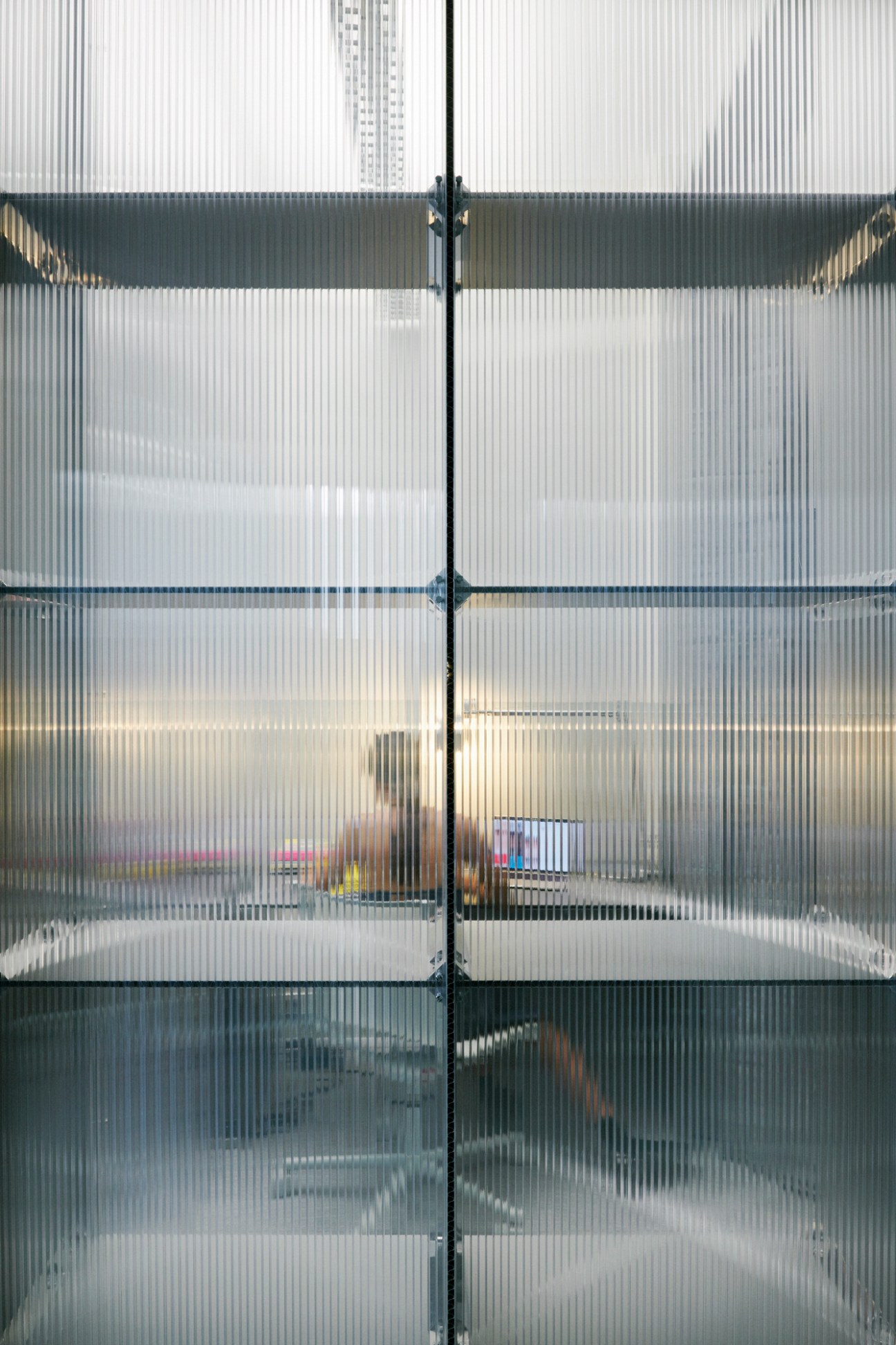 Glass and metal corrugated panels with horizontal dividers creating a modern office partition at Bureau Borsche.