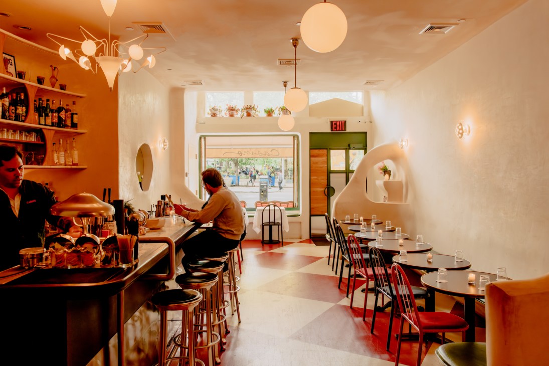 Bright restaurant interior with curved white walls, round bistro tables, red chairs and spherical pendant lights