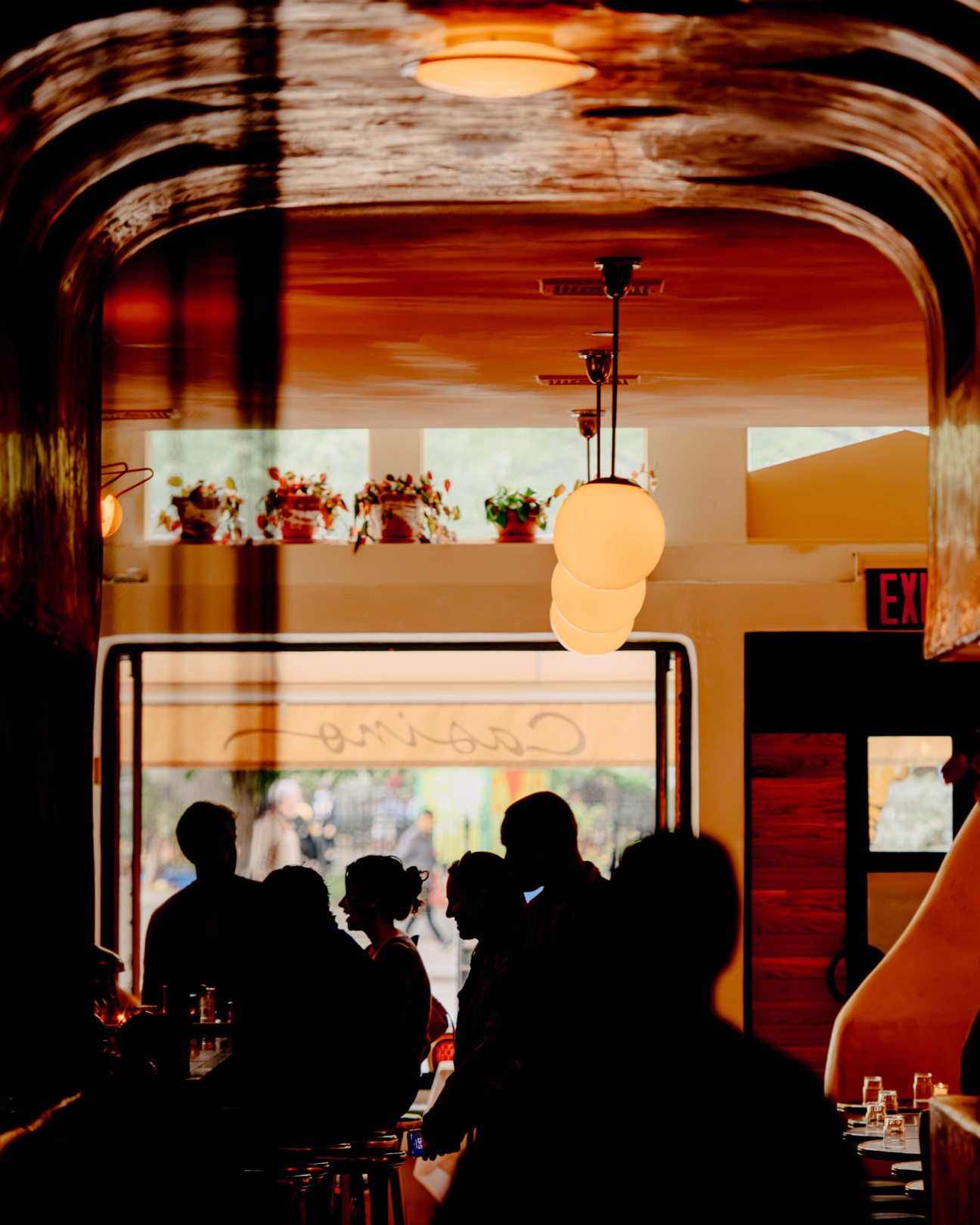 Restaurant interior with silhouetted diners seated at tables under warm pendant lighting and curved ceiling