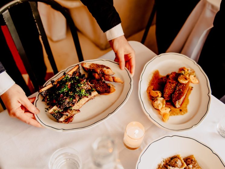 Hands reaching for plated dishes including T-bone steak and pasta at Casino restaurant