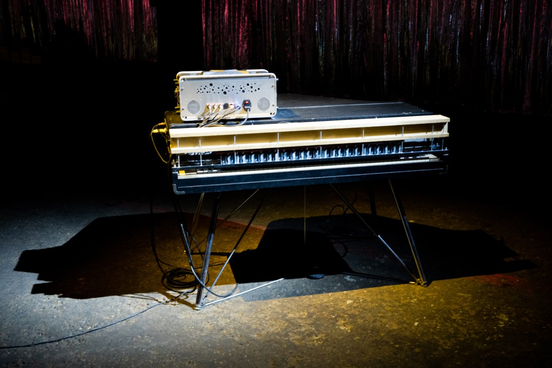 Piano artwork by Charli Tapp displayed in a gallery with industrial brick architecture and colorful streamer backdrop