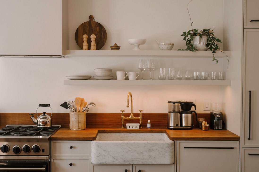 Modern kitchen with white cabinets, wood countertops, marble farmhouse sink, brass faucet and open shelving