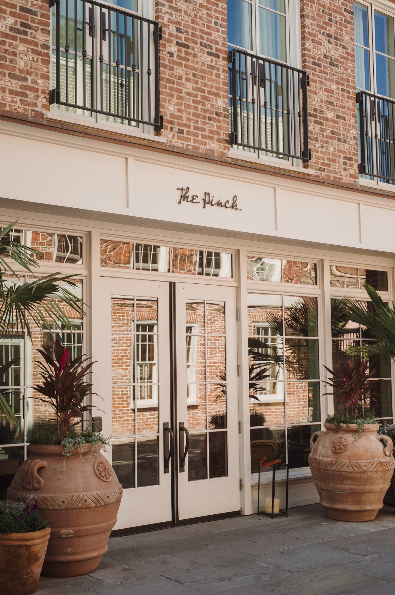 The Pinch hotel entrance with white storefront, glass doors, and decorative planters on brick paved street