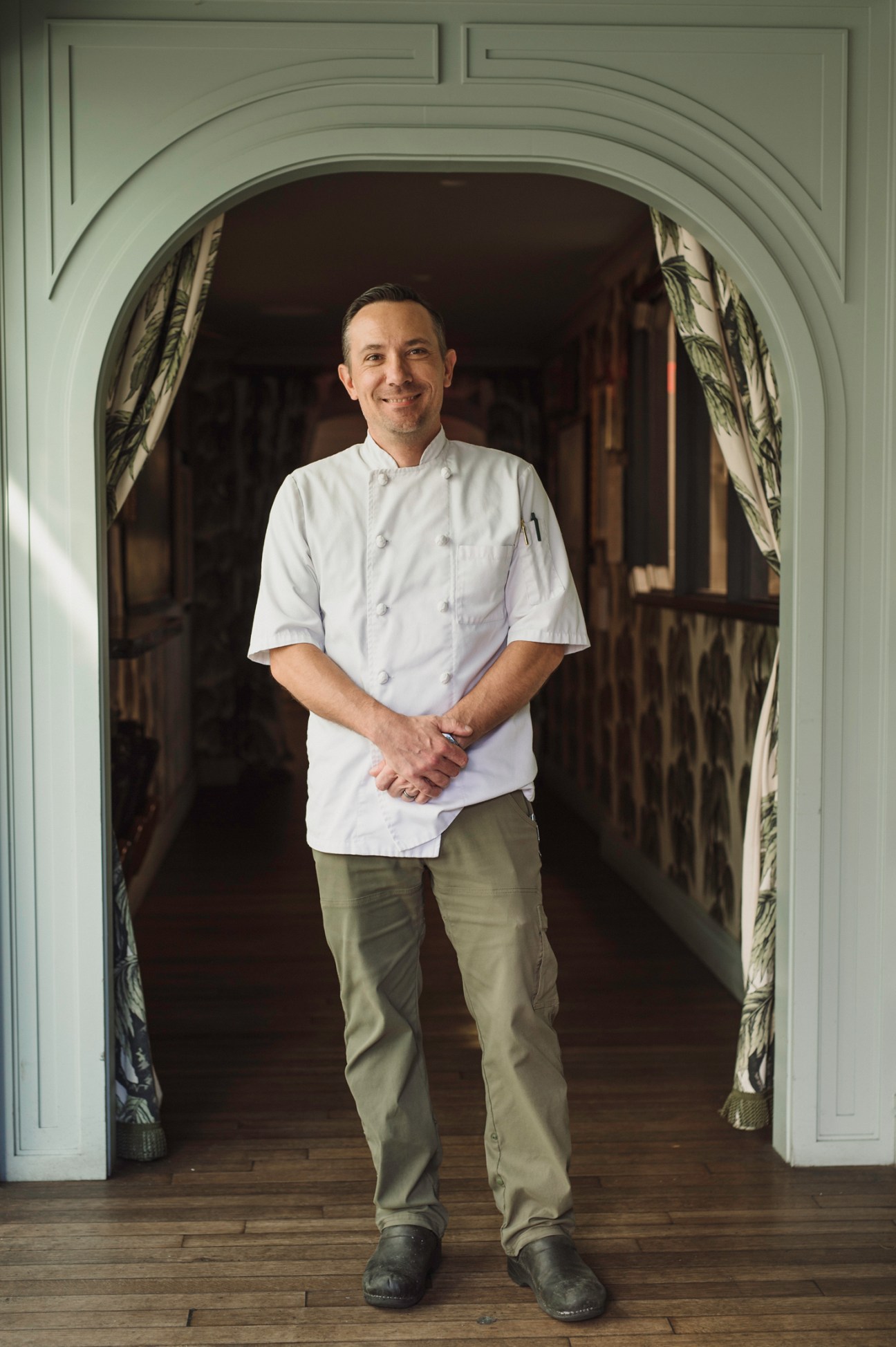 Chef Tim Morton in white chef's coat standing in arched doorway with hands clasped