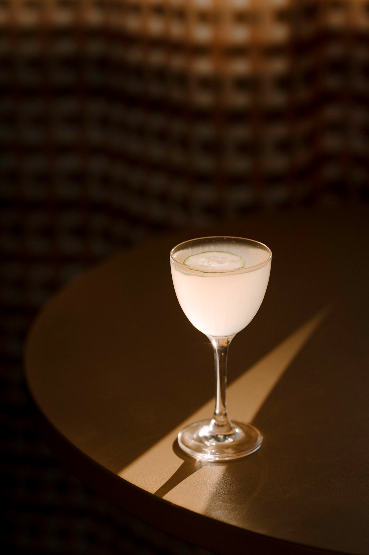 A white cocktail in a coupe glass on a dark surface with dramatic lighting