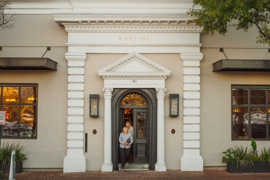 Two people standing in the entrance doorway of Emeline hotel's classical facade with white columns