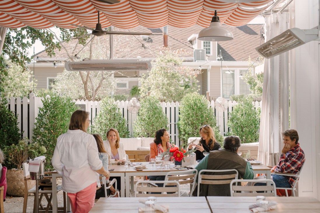 People dining at outdoor restaurant tables under striped awning with pendant lighting